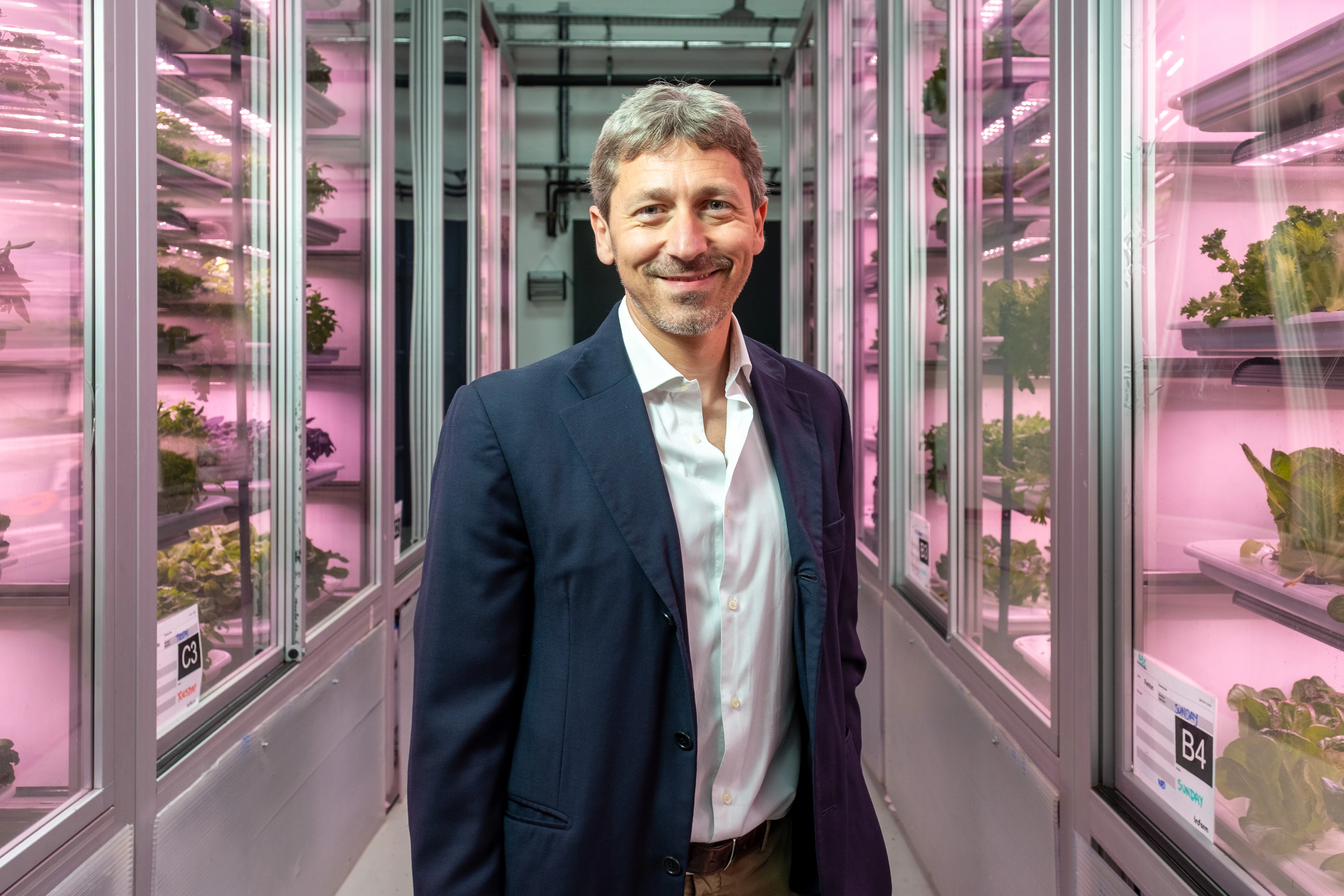 Infarm London Team Photography - Team member in vertical farm corridor, navy blazer, pink grow-light backdrop