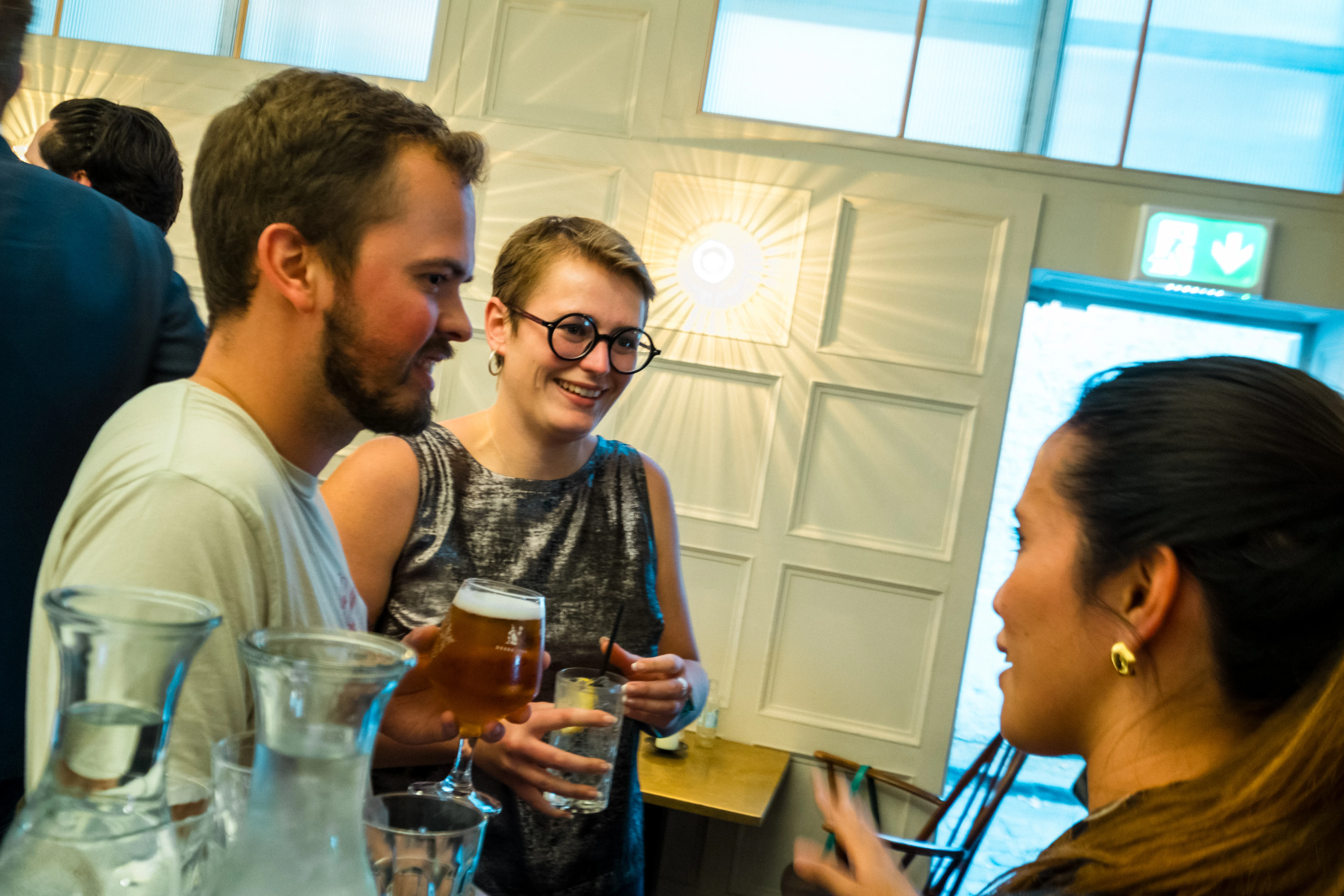 Planet A Ventures Meetup London - Guests laughing over drinks at the bar, panelled wall and sunburst light behind
