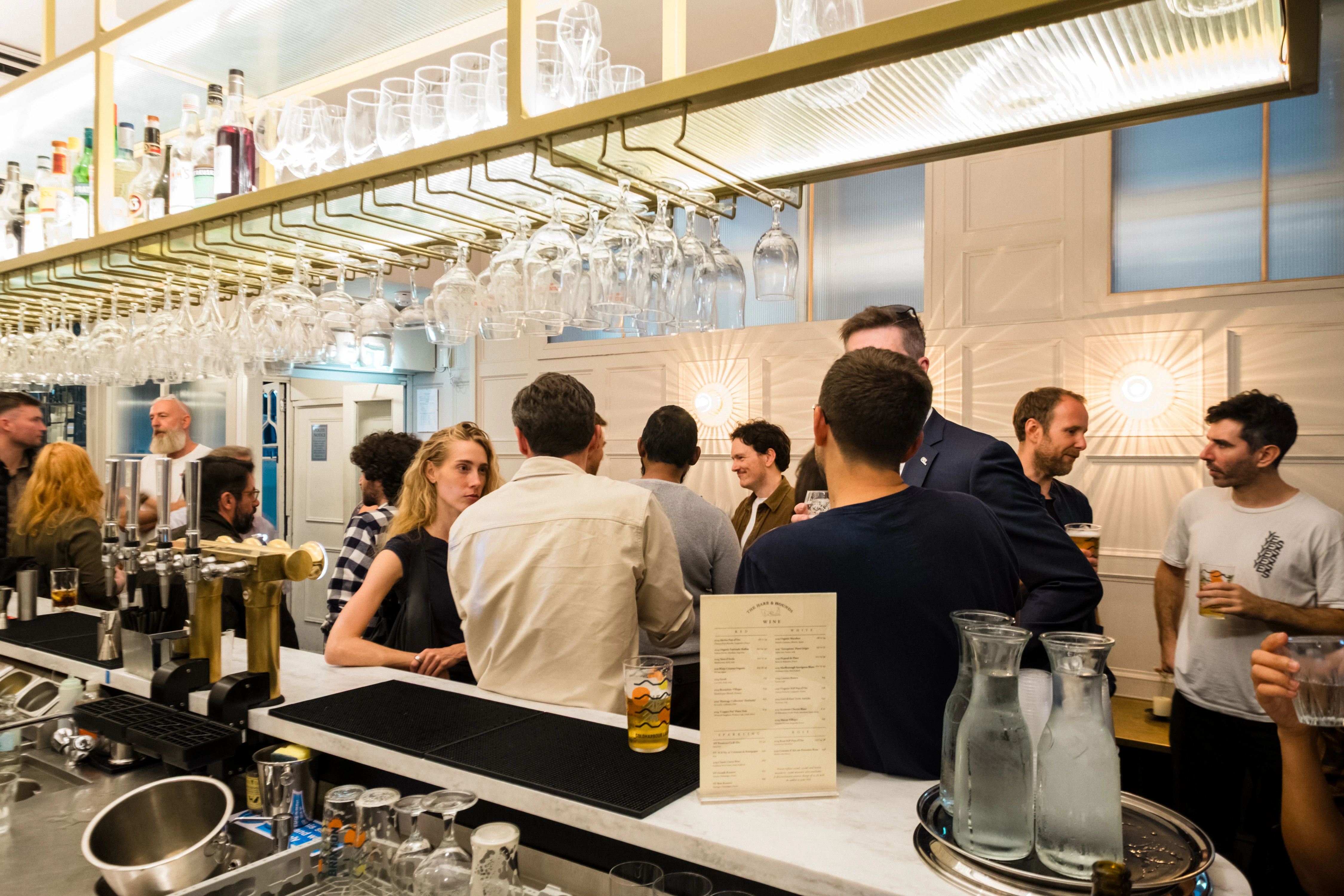Planet A Ventures Meetup London - Guests at the bar counter, brass shelving and menu in frame